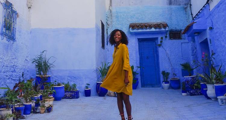 Lächelnde Frau im gelben Kleid posiert im leuchtend blauen Innenhof von Chefchaouen