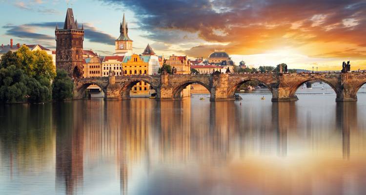 Warmer Sonnenuntergang über der Karlsbrücke in Prag mit klassischer Skyline, die sich in der Moldau spiegelt.
