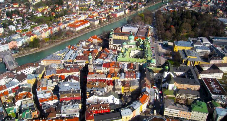 Lebendige Luftaufnahme von Innsbrucks farbenfroher Altstadt entlang des türkisfarbenen Flusses Inn mit alpiner Kulisse.