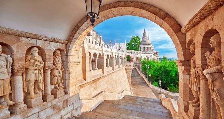 Gewölbte Kolonnade der Fischerbastei in Budapest mit Statuen und konischem Turm mit Blick auf das Grün.