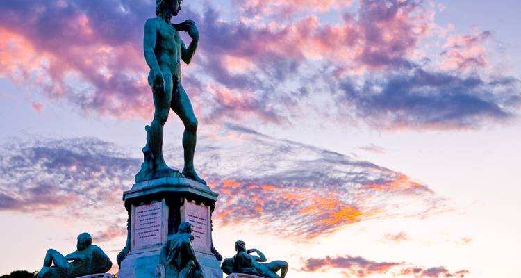 Silhouette of the bronze replica of Michelangelo’s David on its pedestal against a colorful sunset sky.