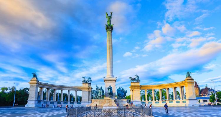 Plaza de los Héroes en Budapest con la columna del Monumento del Milenio y estatuas bajo un cielo azul dramático.