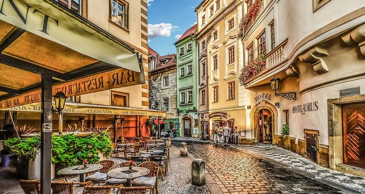 Encantador callejón estrecho con mesas al aire libre, fachadas coloridas y un letrero de hotel boutique en el centro histórico de Praga.