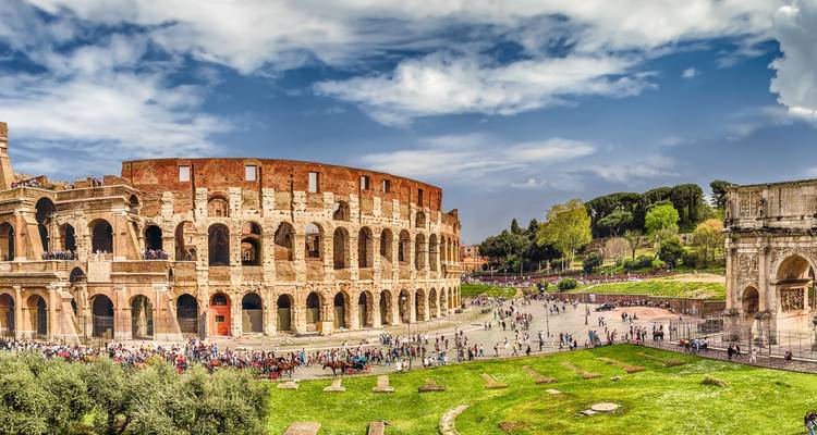 Vasta escena del Coliseo con patio verde y multitudes de turistas disfrutando del clima soleado.