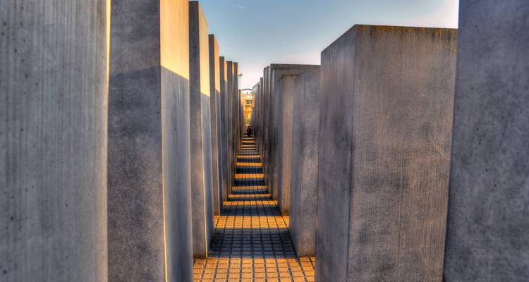 Sendero estrecho entre altas losas de concreto en el Memorial del Holocausto en Berlín con largas sombras.