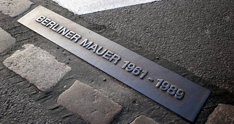 Placa metálica sobre adoquines que marca la antigua ruta del Muro de Berlín.