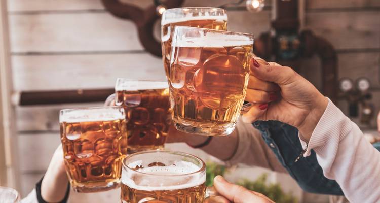 Manos alzando jarras de cerveza espumosa juntas en celebración.