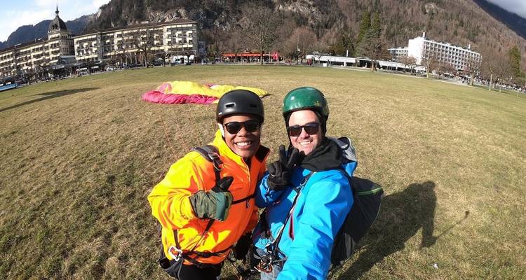 Zwei Männer posieren mit Paragliding-Ausrüstung auf einer grasbewachsenen Wiese.