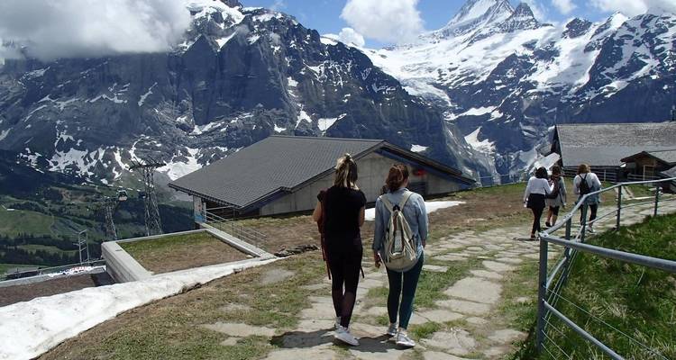 Menschen, die einen Bergpfad entlanggehen, mit schneebedeckten Gipfeln im Hintergrund.