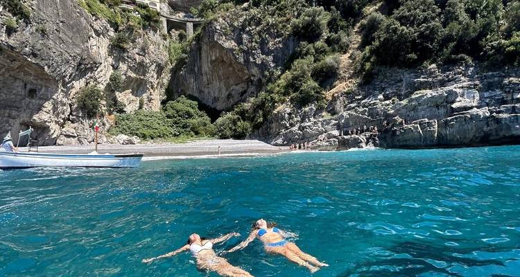 Deux personnes flottant dans une mer turquoise près d'un rivage rocheux.