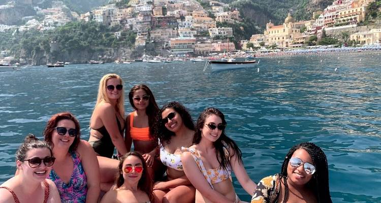 Grupo de personas en un barco con el pueblo de Positano al fondo.