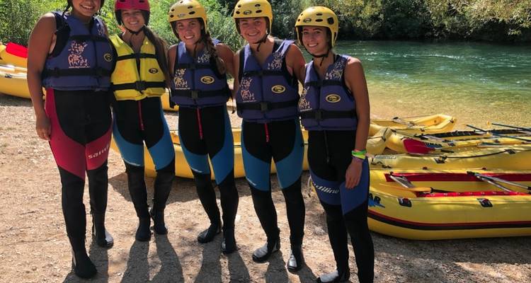 Groupe de personnes en combinaisons de plongée posant pour une photo au bord d'une rivière avec du matériel de kayak.