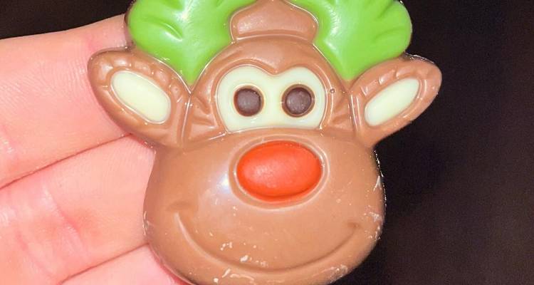 Close-up of a reindeer-shaped milk chocolate candy held between fingers.