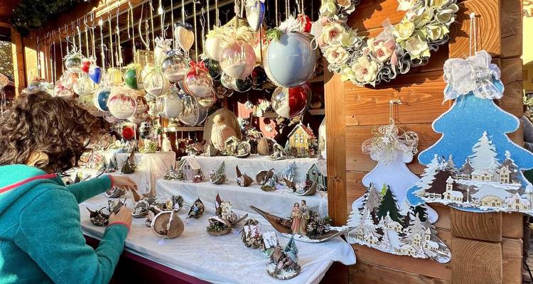 A shopper browses intricately crafted Christmas ornaments at an outdoor wooden stall.