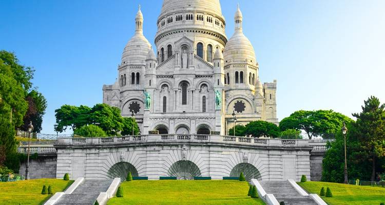 De witte koepels van de Sacré-Cœur Basiliek rijzen boven aangelegde trappen en groene gazons uit.