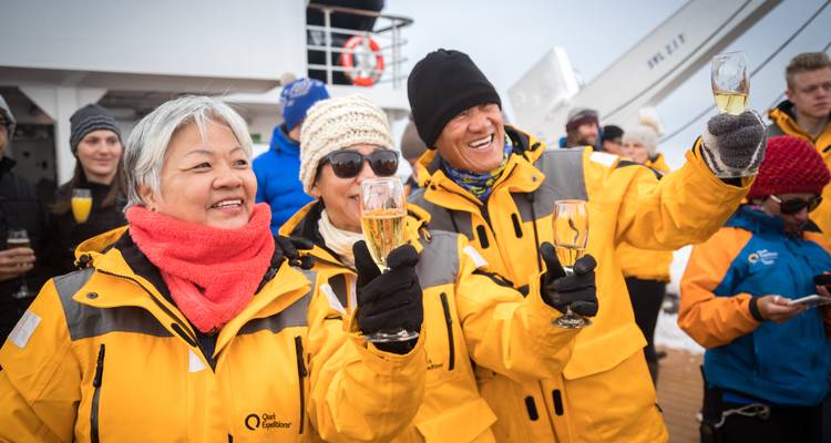 Enveloppés dans des parkas jaunes, les passagers de la croisière lèvent leurs verres de champagne lors d'une célébration polaire sur le pont.