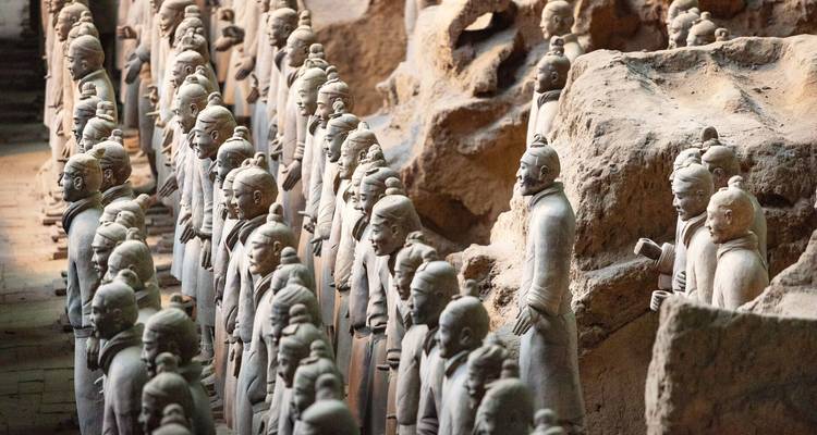 Filas de estatuas de Guerreros de Terracota están de pie en fosas arqueológicas, iluminadas por una suave iluminación interior.