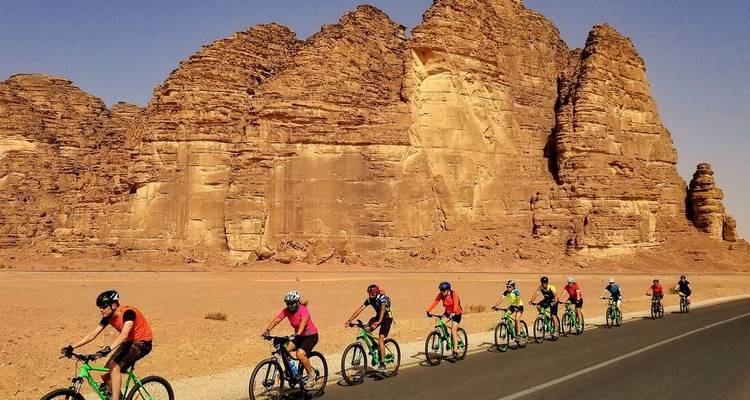 Les cyclistes roulent en file devant d'imposantes formations de grès qui s'élèvent sur une route désertique