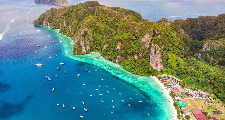 Aerial view of a tropical island with lush greenery and turquoise waters, surrounded by boats.