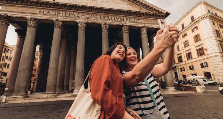 Zwei Freunde machen ein fröhliches Selfie vor dem Pantheon in Rom mit massiven antiken Säulen, die hoch oben aufragen.