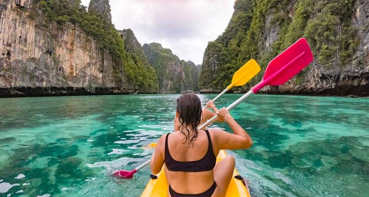 A woman kayaking in clear waters surrounded by cliffs.