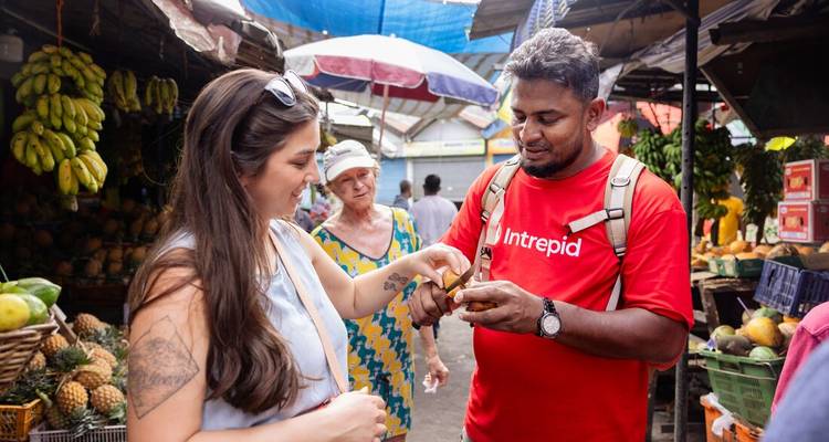Tourists and local guide tasting fruits at a market.