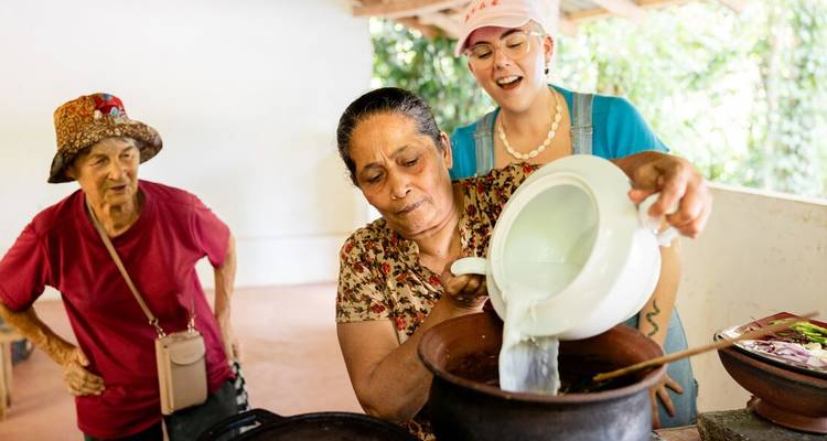 Older woman cooking as a group observes.