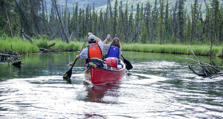 Pareja remando en canoa por un río forestal.