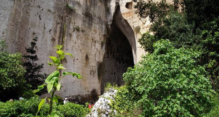 Entrée de grotte rocheuse entourée de verdure.