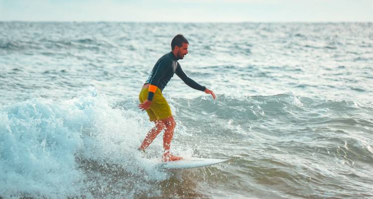 Un surfista monta una ola pequeña, agachado en una tabla en medio de la espuma del mar que brilla.