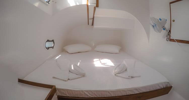 Cabaña compacta de barco blanco con cama doble, portilla y toallas dobladas
