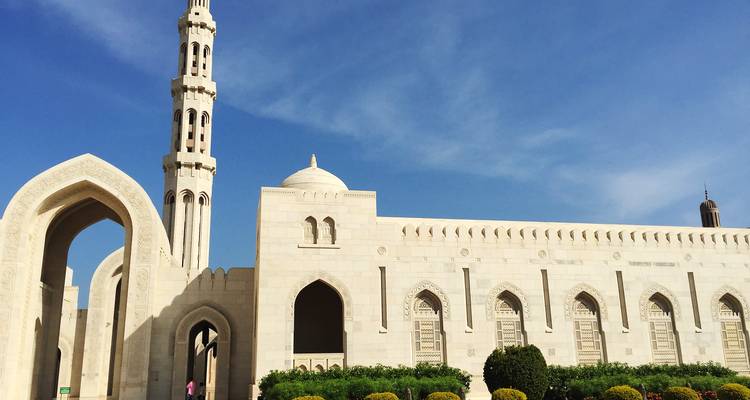 Paredes de mármol blanco impoluto y minarete de la Gran Mezquita del Sultán Qaboos contra un cielo azul brillante.