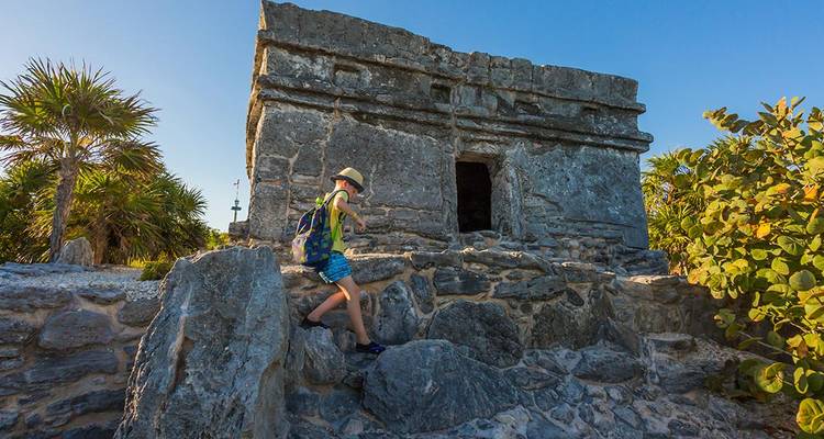 Un voyageur escalade les pierres patinées d'une petite ruine maya sous un ciel bleu limpide du Yucatán.