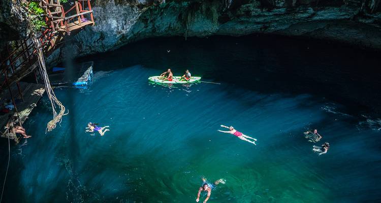 Les nageurs et kayakistes profitent des eaux bleu profond d'un cénote calcaire éclairé par des rayons de soleil.