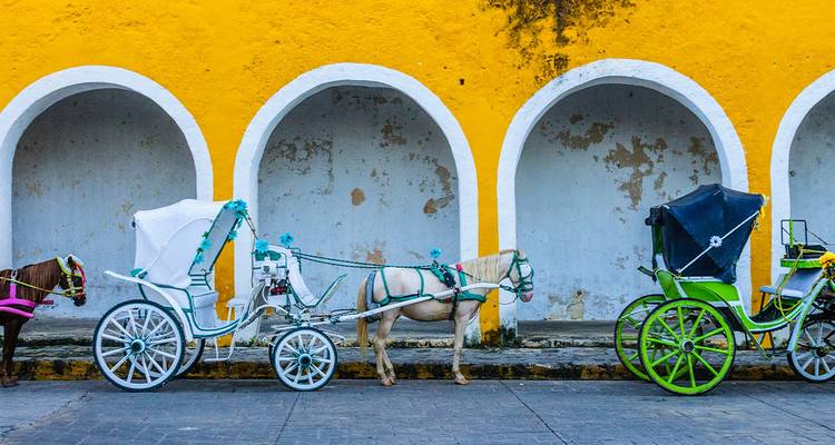 Des calèches colorées s'alignent devant un mur d'arcade jaune vif dans l'Izamal colonial.