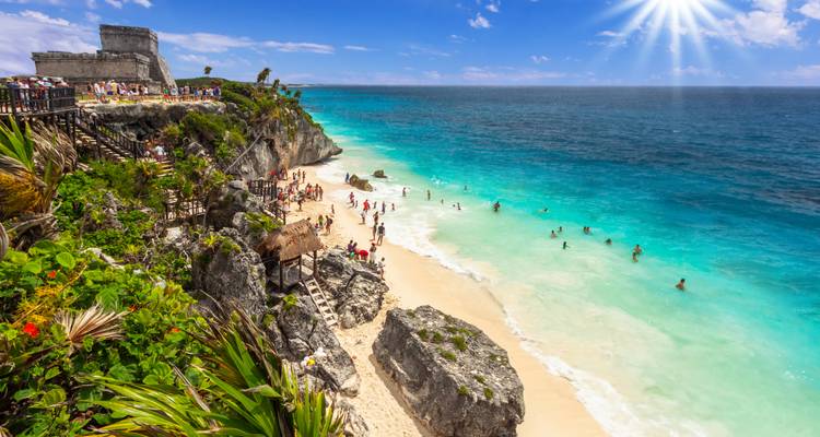 Belebter Strand unterhalb der Tulum-Ruinen, wo Schwimmer das leuchtend türkisfarbene Wasser unter einem strahlenden Sonnenschein genießen.