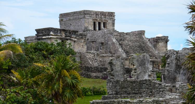 Steinstrukturen und Palmen innerhalb der antiken archäologischen Stätte Tulum an einem ruhigen Tag.