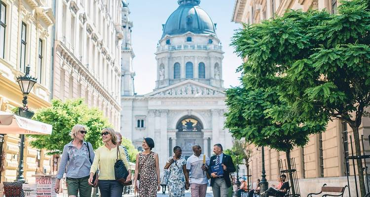 Un petit groupe de touristes se promène le long d'un grand boulevard en direction de la Basilique Saint-Étienne à Budapest.