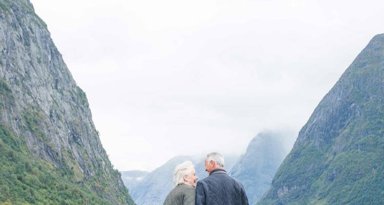 Una pareja mayor se encuentra entre altas paredes de fiordo, compartiendo un momento silencioso entre picos brumosos.