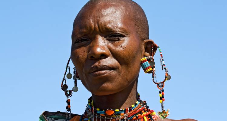 Retrato de una mujer maasai adornada con coloridas joyas de cuentas contra un cielo azul claro.