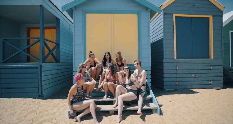 Groupe de personnes assises sur les marches de cabines de plage colorées.