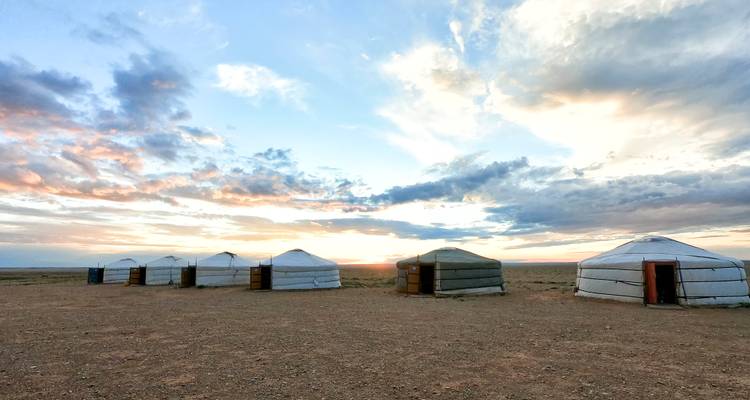 Una fila de gers blancos (yurtas) se alza en las llanuras desérticas abiertas bajo un cielo de atardecer colorido.