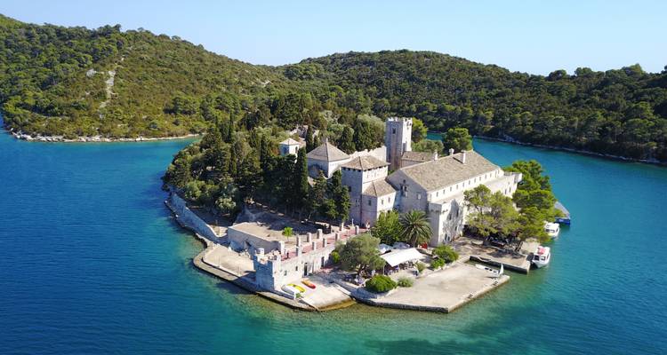 Monasterio histórico en una isla rodeada de mar y bosque.