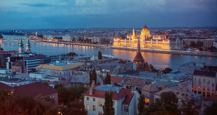 Panorama crépusculaire de Budapest avec le Parlement hongrois illuminé se reflétant dans le Danube.