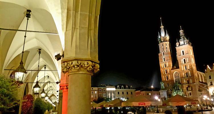 Nighttime arcade view framing Krakow's main square with St. Mary's twin towers lit up