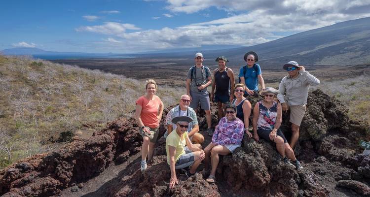 Group of travellers poses on rugged lava rocks with expansive volcanic landscape and clouds in the background.