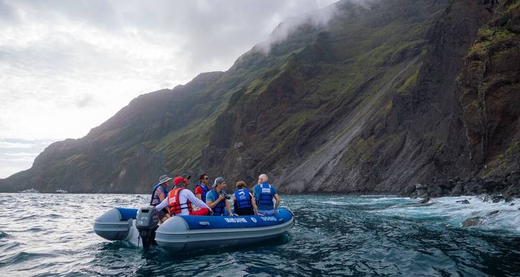 Turistas en un bote auxiliar en aguas oceánicas cerca de acantilados empinados.