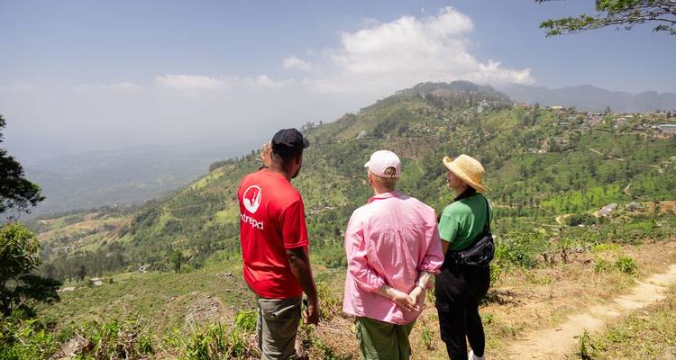 Drie wandelaars pauzeren bij een heuveltop uitkijkpunt met uitzicht over Sri Lanka's groene hooglanden.