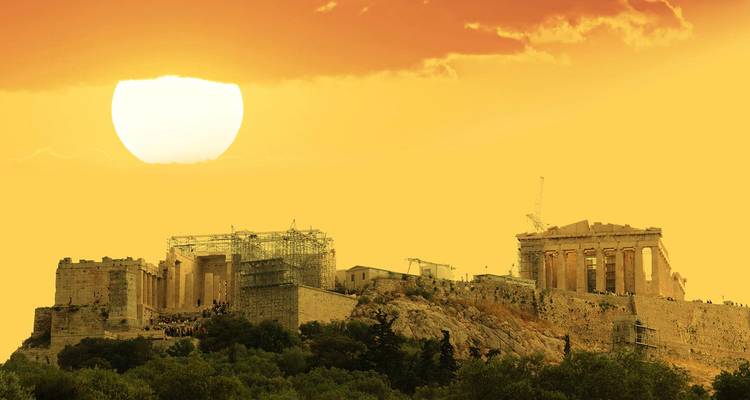 Las ruinas del Partenón y la Acrópolis recortadas contra una puesta de sol de color naranja brillante con un sol grande y bajo en el cielo.