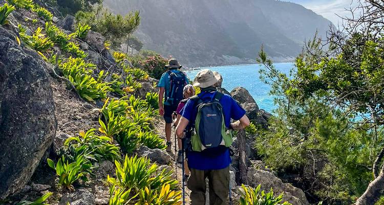Excursionistas con mochilas caminan por un sendero costero exuberante que ofrece vistas a un agua turquesa brillante